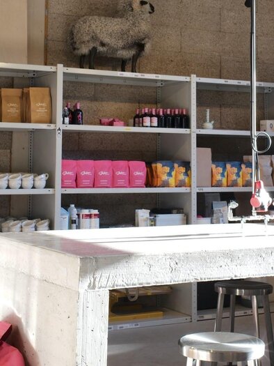 Ein moderner Raum mit Regalen, die verschiedene Produkte wie Kosmetika und Lebensmittel enthalten. In der Mitte steht ein großer Tisch aus Beton.