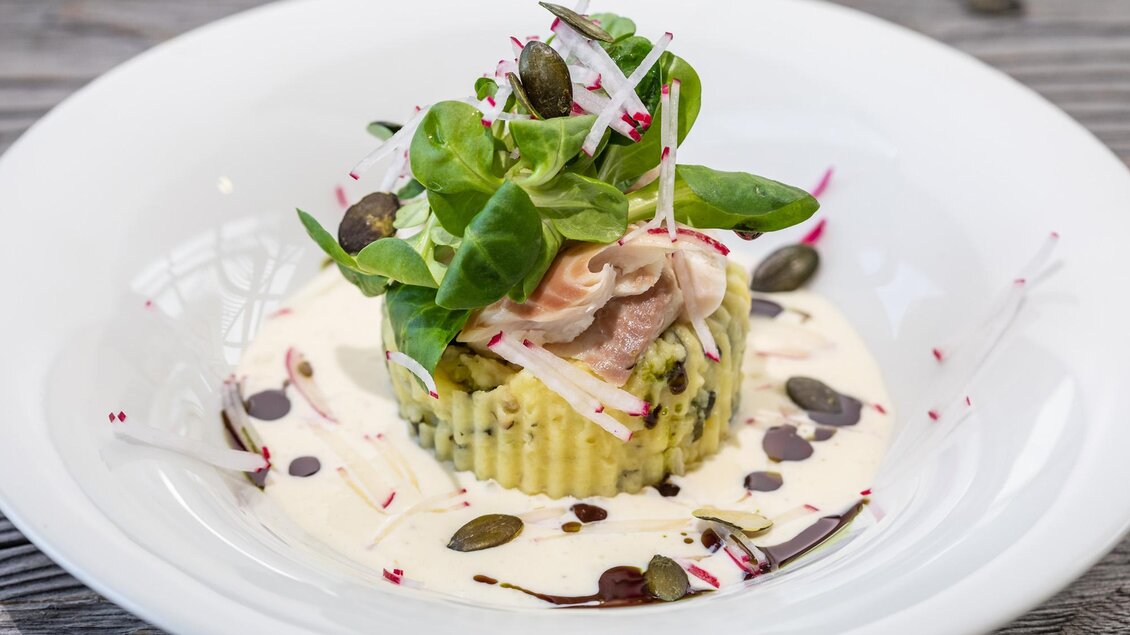 Ein delikates Gericht auf einem weißen Teller. Es besteht aus einer Schicht Gemüse mit Salat, Radieschen und einer cremigen Sauce. | © Seewigtal Stüberl