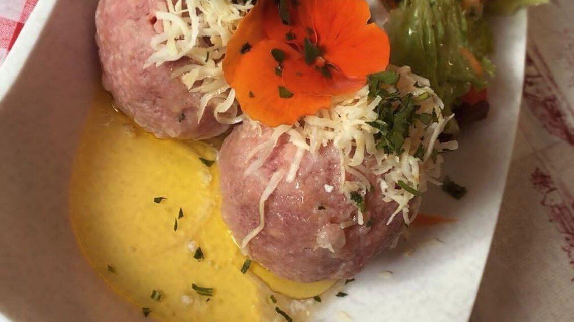 Ein Teller mit zwei großen Fleischbällchen in einer Soße, garniert mit Käse und einer Blume. Daneben liegt ein frischer Salat mit verschiedenen Gemüsesorten. | © Spechtenseehütte