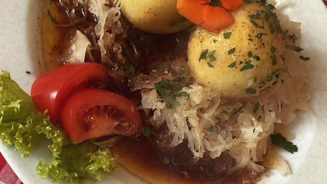Ein Teller mit Sauerkraut, zwei Knödeln und einer Beilage aus frischem Gemüse. Der Hintergrund ist mit kariertem Tischdeckenmuster dekoriert. | © Spechtenseehütte