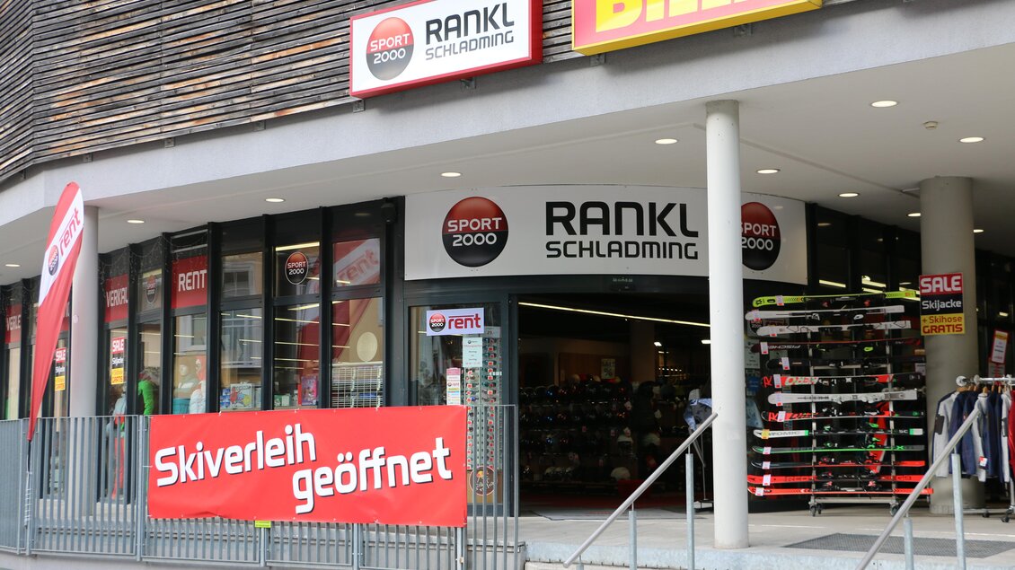 Ein Sportgeschäft mit der Aufschrift "RANKL Schladming" und einem großen Banner, das "Skiverleih geöffnet" verkündet. Im Schaufenster sind Ski und Sportartikel ausgestellt. | © Sport 2000 Rankl Schladming