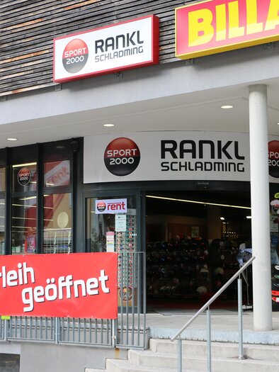 Ein Sportgeschäft mit der Aufschrift "RANKL Schladming" und einem großen Banner, das "Skiverleih geöffnet" verkündet. Im Schaufenster sind Ski und Sportartikel ausgestellt. | © Sport 2000 Rankl Schladming