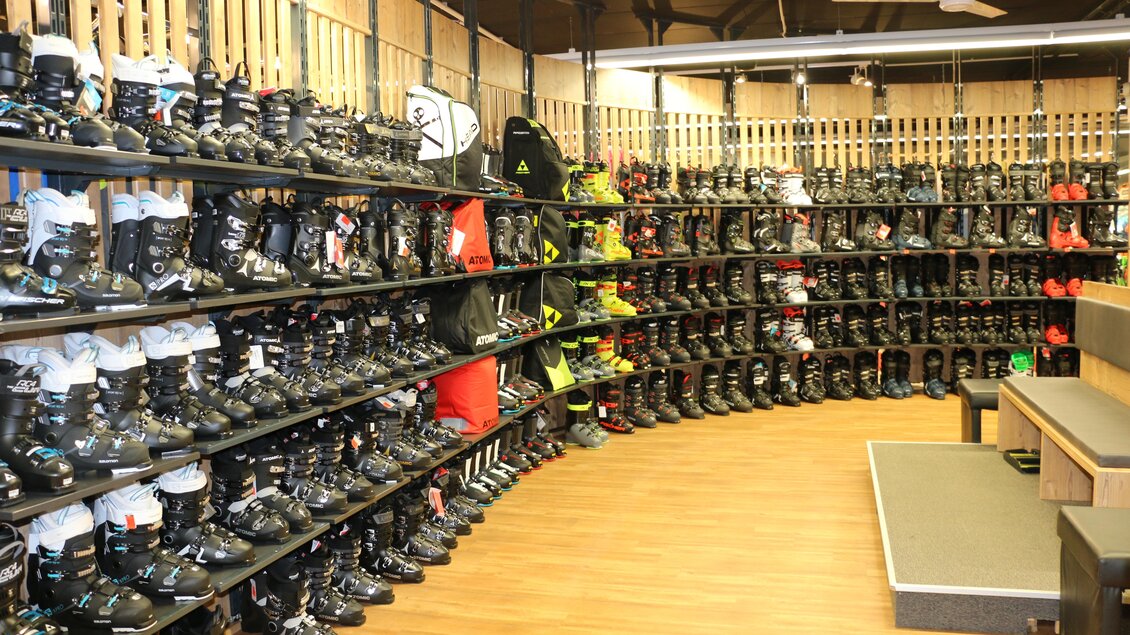 Ein sportliches Geschäft mit Regalen voller Skischuhe in verschiedenen Größen und Farben. Die Wände sind aus Holz, und der Boden ist aus hellem Holzdesign. | © Sport 2000 Rankl Schladming