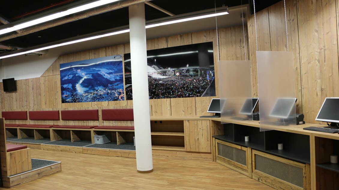 Ein moderner Innenraum mit Holzverkleidung und Computerarbeitsplätzen. An der Wand hängt ein großes Bild einer Menschenmenge in einer Veranstaltung. | © Sport 2000 Rankl Schladming