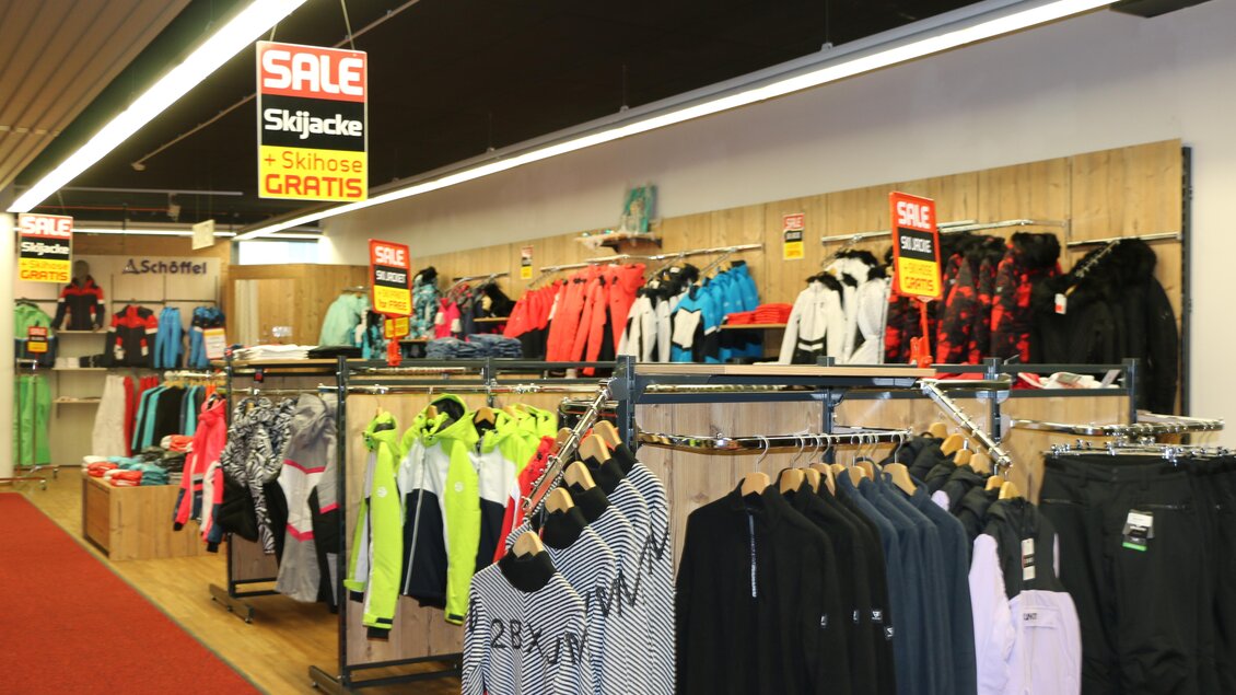 Ein Verkaufsraum mit verschiedenen Sportbekleidungen. Über den Regalen hängen Preisschilder, die auf Sonderangebote hinweisen. | © Sport 2000 Rankl Schladming