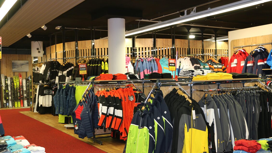 Ein Geschäft für Sportbekleidung mit Regalen voller Ski- und Outdoorbekleidung. Die Farben variieren von Schwarz und Blau bis zu leuchtenden Gelbtönen und Rot. | © Sport 2000 Rankl Schladming