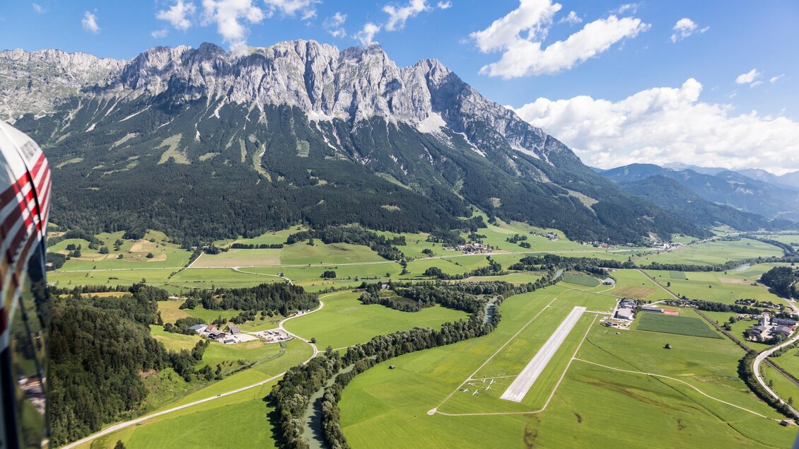 Eine beeindruckende Berglandschaft mit grünen Wiesen und einem klaren blauen Himmel. Am Fuße der Berge ist eine Landebahn zu sehen. | © Sportsarea Grimming
