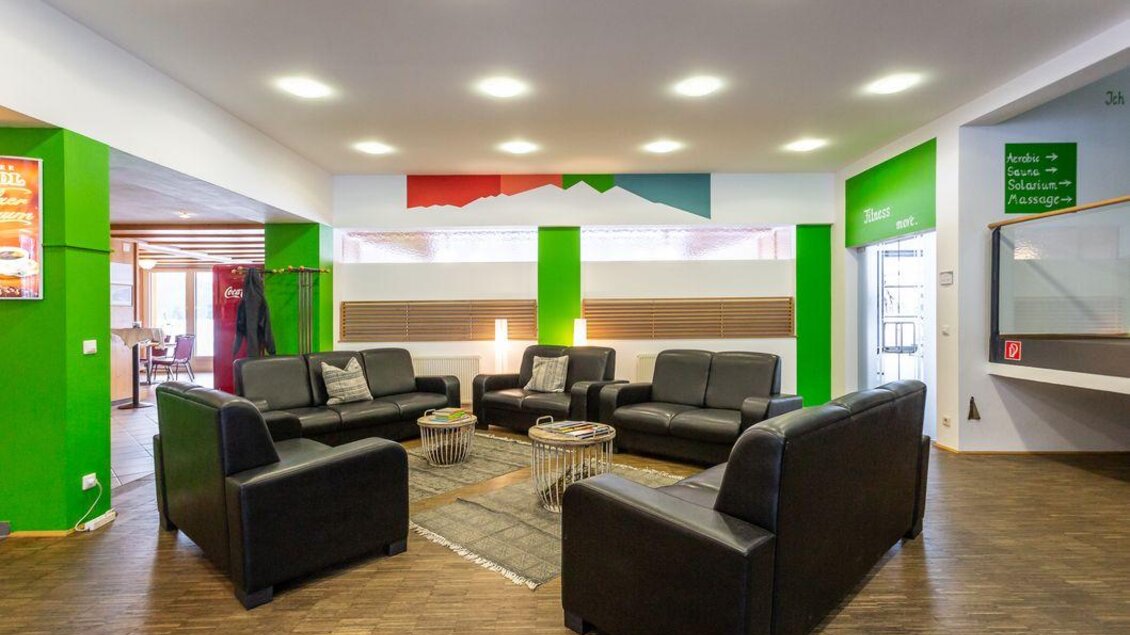 Ein modernes Lounge-Bereich mit schwarzen Sofas und einem runden Tisch. Die Wände sind in hellen Farben mit grünen Akzenten gestaltet. | © Sportsarea Grimming