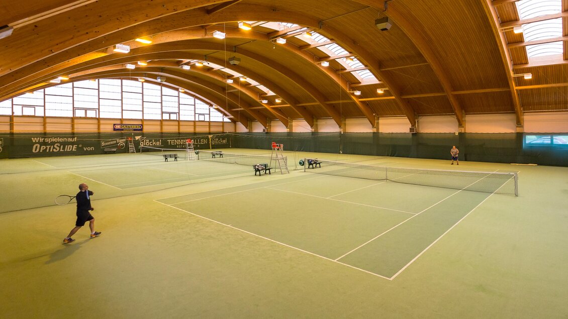 Eine geräumige Tennis-Halle mit Holzdecke und mehreren Spielfeldern. Ein Spieler ist gerade im Training. | © Sportsarea Grimming