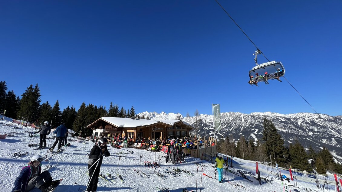 Eine Skilandschaft mit vielen Skifahrern und einer Bergstation. Im Hintergrund sind schneebedeckte Berge und ein klarer blauer Himmel zu sehen. | © Stöcklhütte