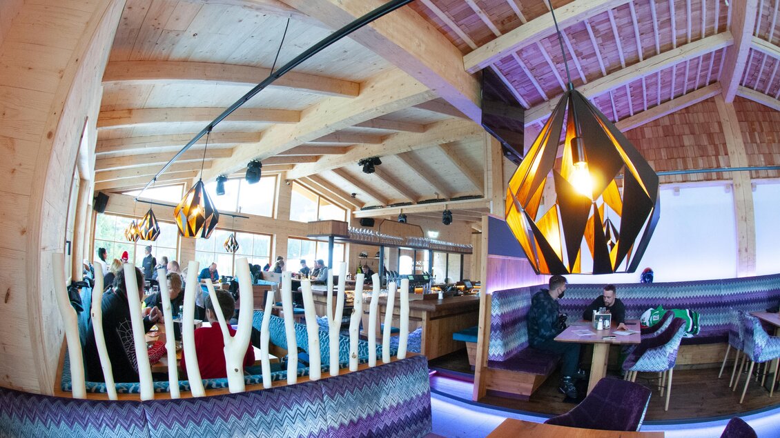 Ein modernes Restaurant mit Holzdekor und bunten Lampen. Im Innenraum sitzen Gäste an Tischen und genießen ihre Zeit. | © Stöcklhütte