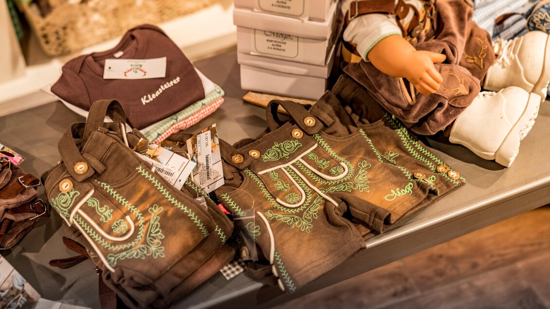 Eine Auslage mit traditionellen Lederhosen für Kinder. Auf dem Tisch liegen auch Kleidung und Spielzeug. | © Steirerland Tracht & Leder