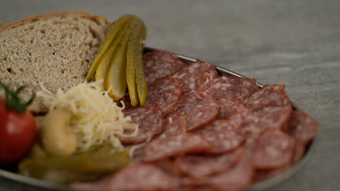Ein Teller mit Wurst, frischem Brot und eingelegtem Gemüse. Dazu liegen einige Tomaten und Sauerkraut. | © Perner Alexandra