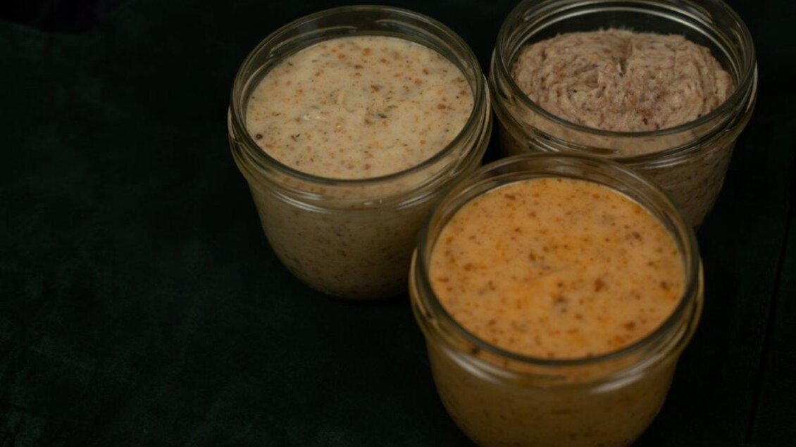 Drei Gläser mit verschiedenen Pasten in neutralen Farben stehen auf einem dunklen Hintergrund. Die Texturen der Pasten sind cremig und einladend. | © Perner Alexandra