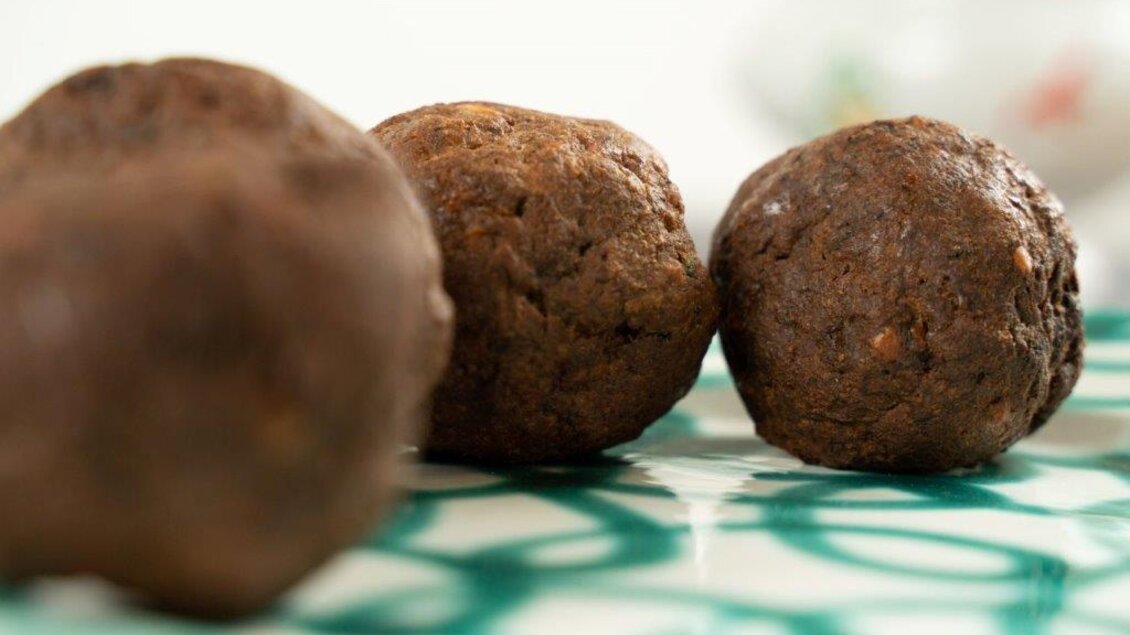 Drei runde, dunkle Bällchen liegen auf einem gemusterten Untergrund. Die Bällchen wirken appetitlich und knusprig. | © Perner Alexandra
