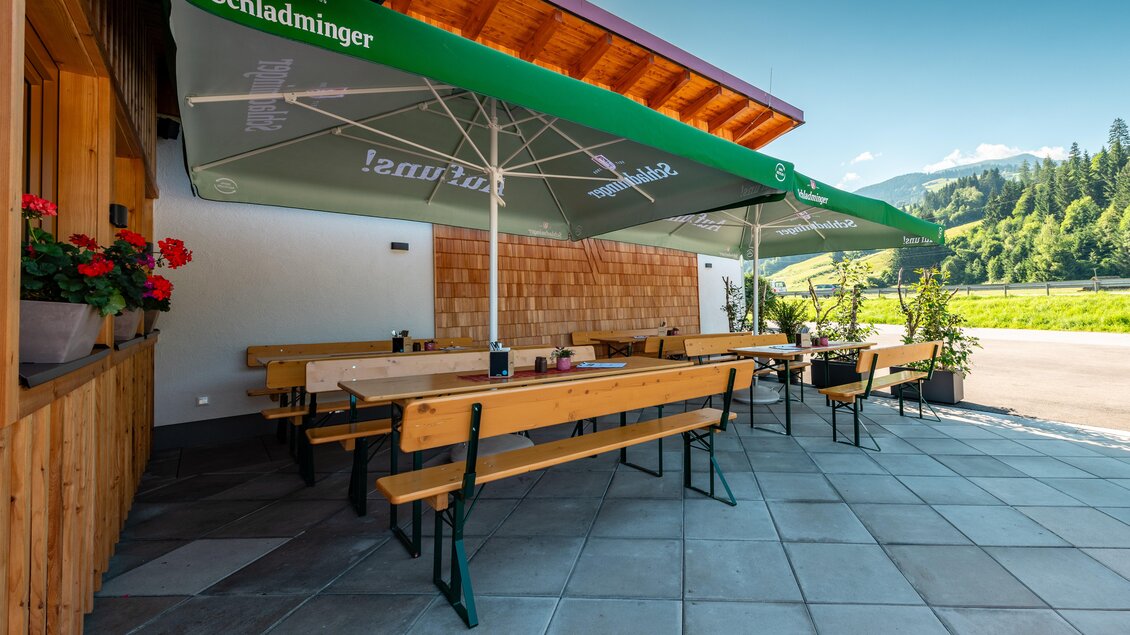 Eine einladende Terrasse mit Holzbank und Markisen. Im Hintergrund sind die Berge und der blaue Himmel sichtbar. | © Steirische Hendlstub'n