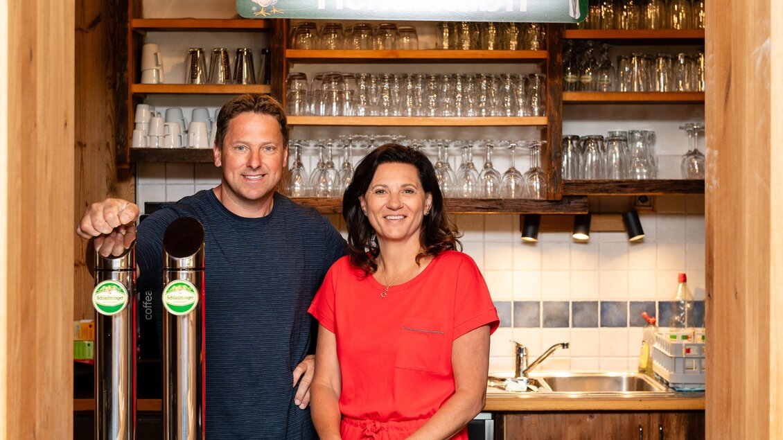 Ein freundliches Paar steht hinter einer Bar. Es gibt Zapfhähne und viele Gläser im Hintergrund. | © Steirische Hendlstub'n