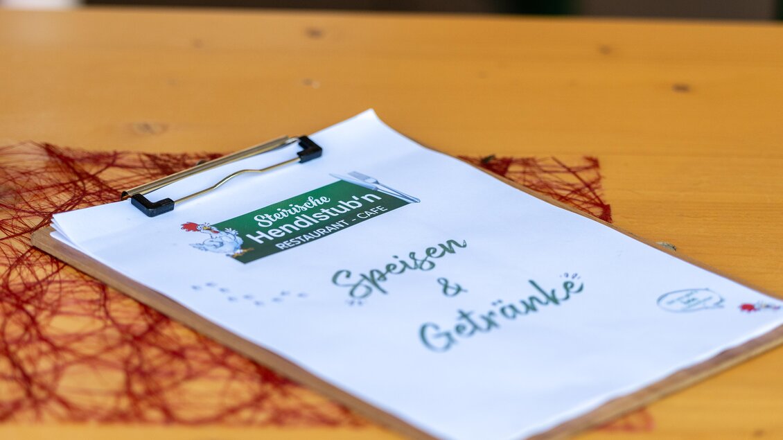 Ein Speisekartenblatt auf einem Holztisch. Es ist beschriftet mit "Speisen & Getränke". | © Steirische Hendlstub'n