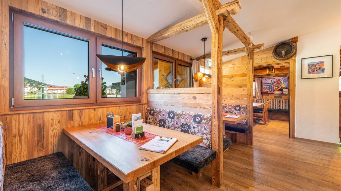 Eine gemütliche Innenansicht eines Restaurants mit Holzelementen. Am Tisch liegen Menüs und die Fenster bieten einen Blick nach draußen. | © Steirische Hendlstub'n