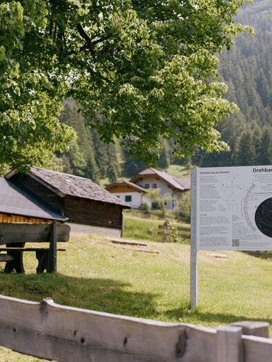 A picturesque landscape with an informative panel about the star map. In the background, wooden houses and trees can be seen. | © Gerald Grünwald