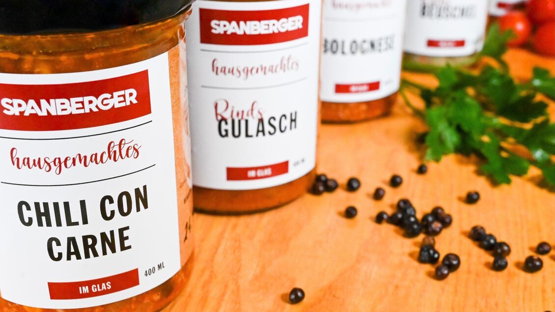 Mehrere Gläser mit hausgemachten Gerichten stehen auf einem Holztisch. Die Etiketten sind gut lesbar und zeigen verschiedene Sorten wie Chili con Carne und Rindergulasch. | © Andreas Spanberger