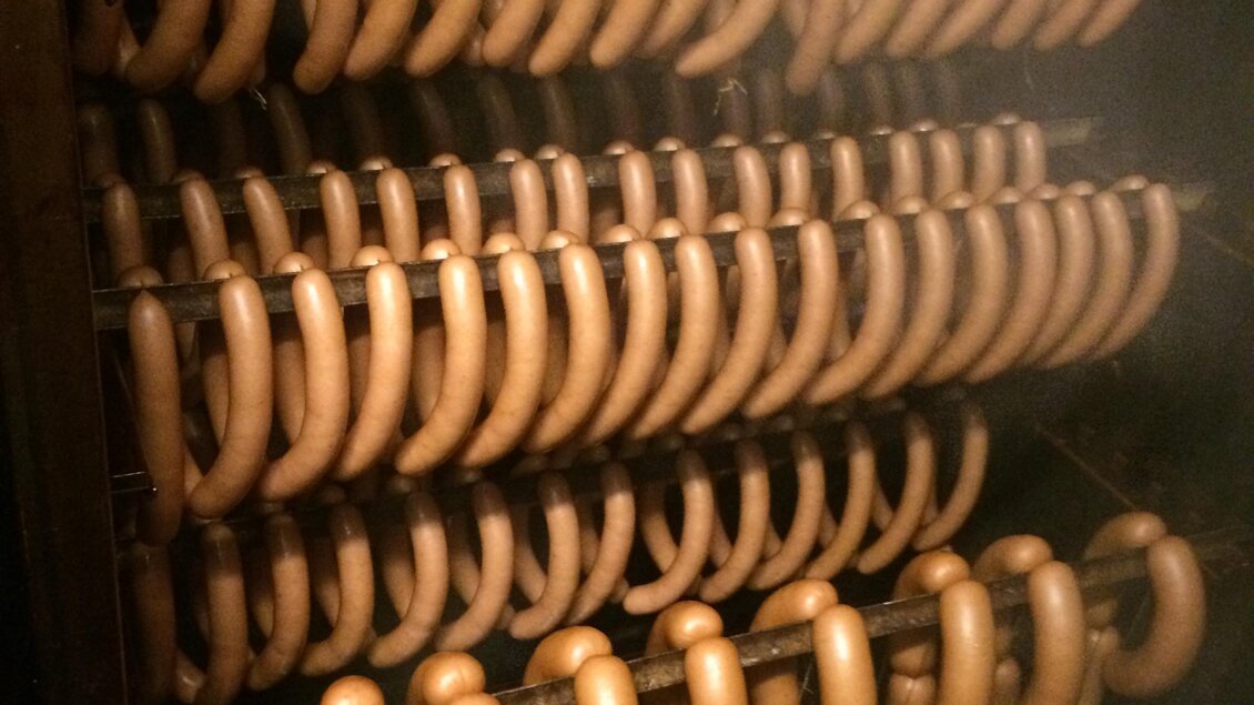 Eine Reihe von geräucherten Würstchen hängt in einem Räucherofen. Die Würstchen haben eine goldbraune Farbe und sind ordentlich aufgereiht. | © Andreas Spanberger