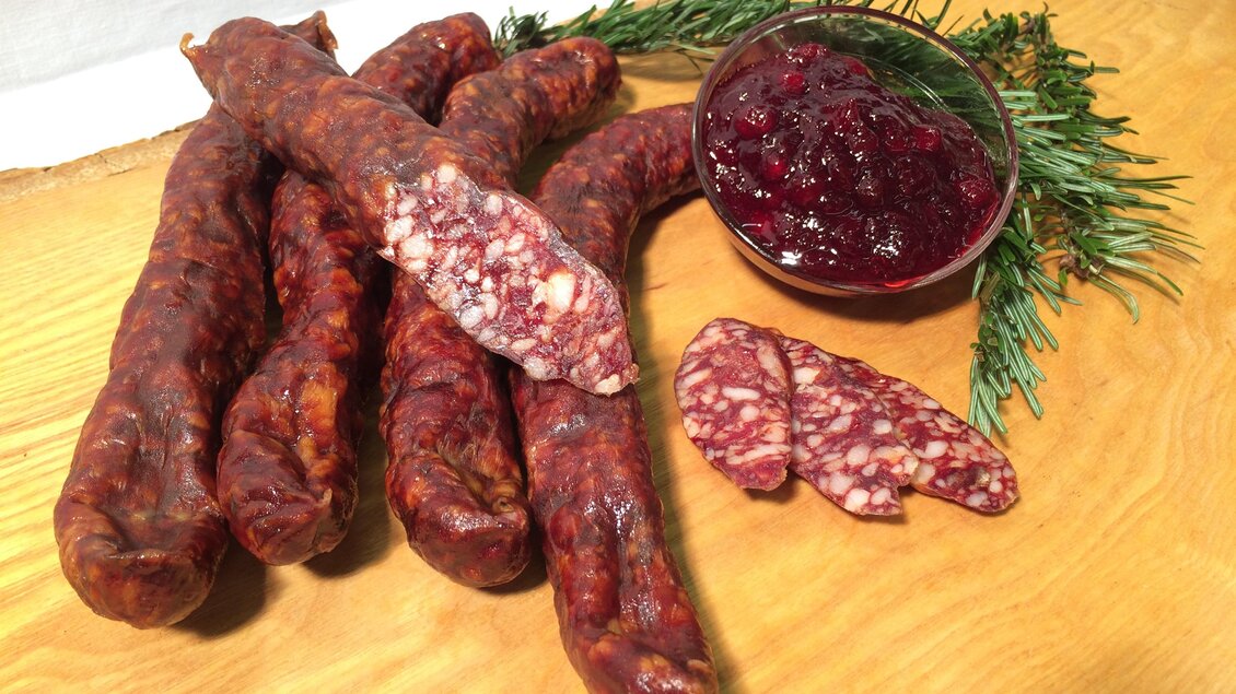 Eine Auswahl von Wurststücken liegt auf einem Holztisch. Dazu gibt es ein Glas mit Marmelade und etwas grüne Dekoration. | © Andreas Spanberger
