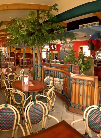 Ein gemütliches Restaurant mit Holzdekor und vielen Pflanzen. Die Tische sind mit Stühlen im traditionellen Stil ausgestattet. | © Strandcafe Putterersee