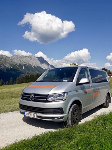 Ein silberner VW-Taxi-Van steht auf einem Schotterweg in einer malerischen Berglandschaft. Die Wolken am blauen Himmel verleihen der Szene einen entspannenden Eindruck. | © Claudia Seebacher