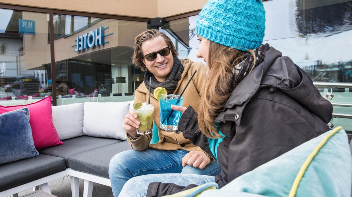 Zwei Personen genießen alkoholfreie Cocktails auf einer gemütlichen Terrasse. Im Hintergrund ist das Hotel zu sehen. | © TUI BLUE