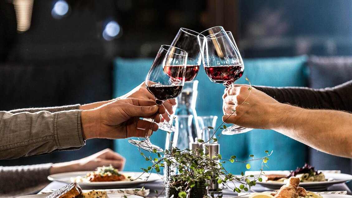 Ein festlicher Tisch mit köstlichem Essen und Gläsern Rotwein, die in einem Toast angehoben werden. Die Atmosphäre ist warm und einladend. | © TUI BLUE