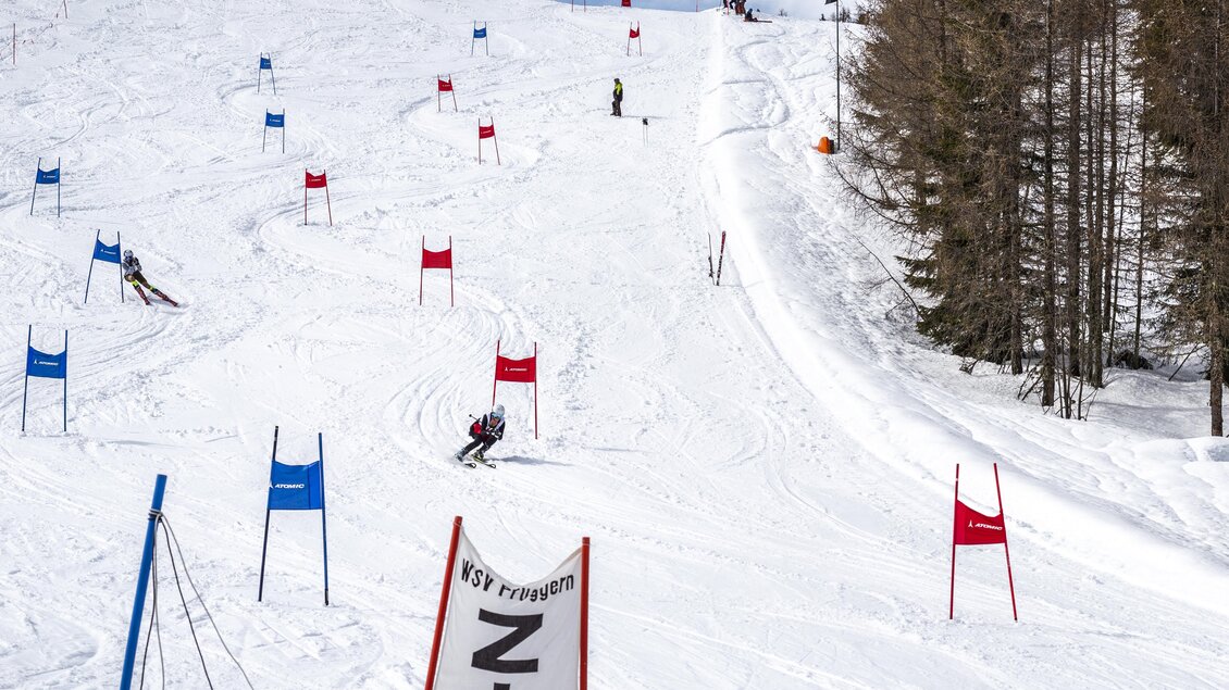 Eine schneebedeckte Piste mit roten und blauen Toren für Skirennen. Skifahrer bewegen sich talwärts zwischen den Toren in einer sonnigen Winterlandschaft. | © Galsterberg/David Stocker