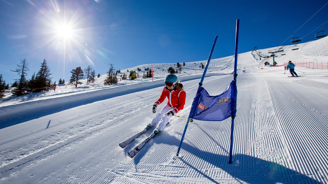 Ein Skifahrer fährt eine präparierte Piste entlang, umgeben von Schnee und Bäumen. Der Himmel ist klar und die Sonne strahlt hell. | © Tom Lamm