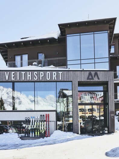 A modern building with the inscription "VEITHSPORT" in a snow-covered environment. In the background, mountains and a blue sky are visible. | © ARX Boutique Hotel