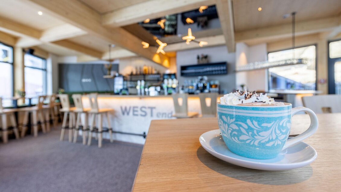 Eine gemütliche Café-Umgebung mit einem blauen Becher Kaffee auf einem Tisch. Im Hintergrund ist die Bar gut sichtbar. | © Harald Steiner