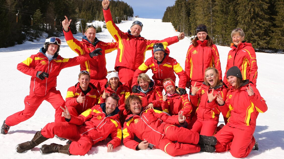 Eine Gruppe von Skilehrern posiert fröhlich im Schnee. Sie tragen rote Skijacken und zeigen verschiedene Gesten. | © WM-Schischule Royer