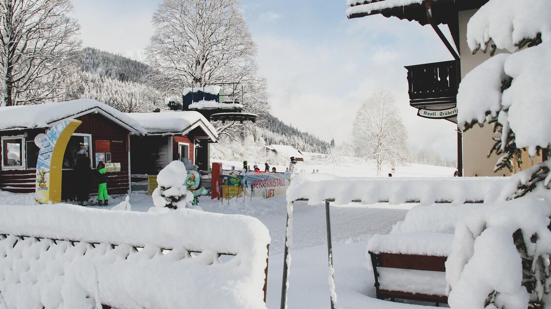 Eine verschneite kleine Hütte steht rechts von einem ebenfalls eingeschneitem Haus. Im Vordergrund ist ein in Schnee gedeckter Zaun. | © Foto Tom
