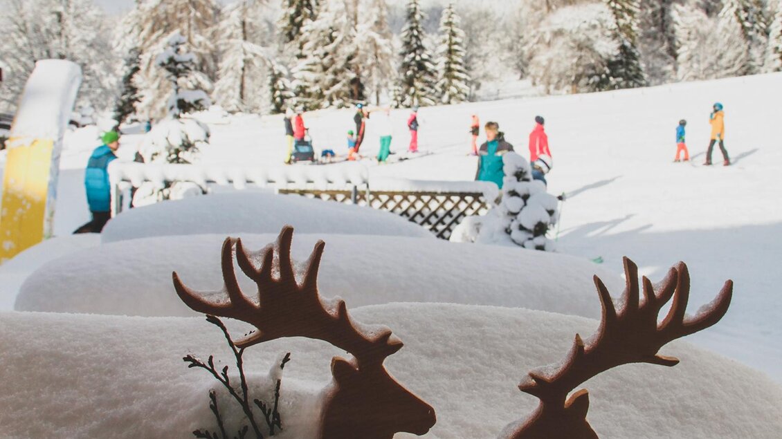 Im Vordergrund sind zwei kleine Deko Rehntiere eingeschneit. Im Hintergrund ist das verschneite Kinder-Skiland und blauer Himmel zu sehen. | © Foto Tom