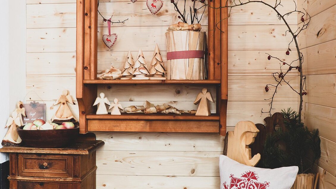Kleiner, liebevoll dekorierter Bereich mit Holzregal, Weihnachtsdekoration, Äpfeln im Korb und Kissen mit rotem Muster. | © Foto Tom