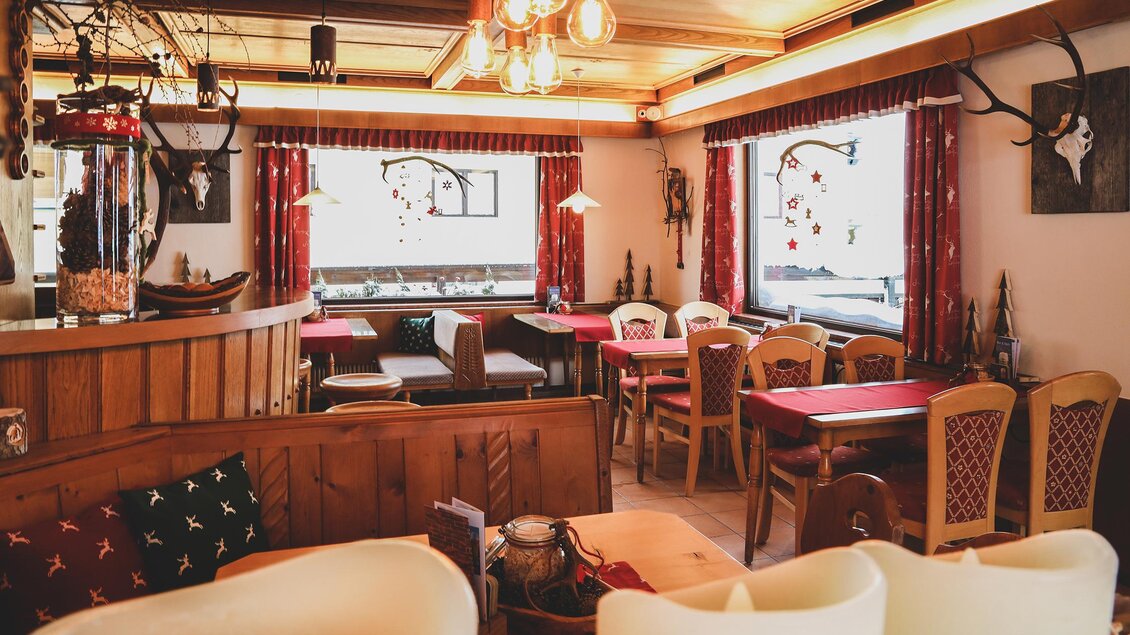 Gemütliches Gasthaus mit Holzdecke, roten Vorhängen und festlich gedeckten Tischen – warme, einladende Atmosphäre. Im Vordergrund sind weiße Kerzen aufgestellt. | © Foto Tom