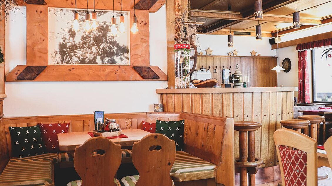 Gemütliche Stube mit Holzmöbeln, einer Sitzecke mit bunten Kissen und einem großen historischen Foto an der Wand. | © Foto Tom