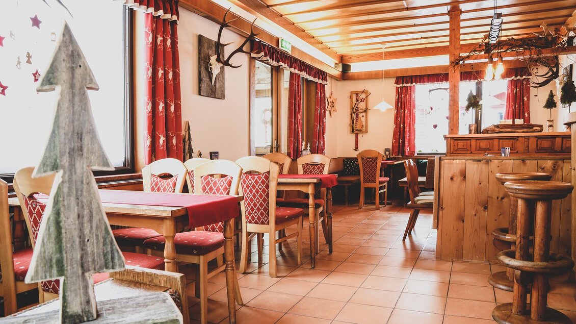 Gemütliches Gasthaus mit Holzdecke, roten Vorhängen und festlich gedeckten Tischen – warme, einladende Atmosphäre. In der linken Bildhälfte ist ein Baum aus grauem Filz aufgestellt. | © Foto Tom
