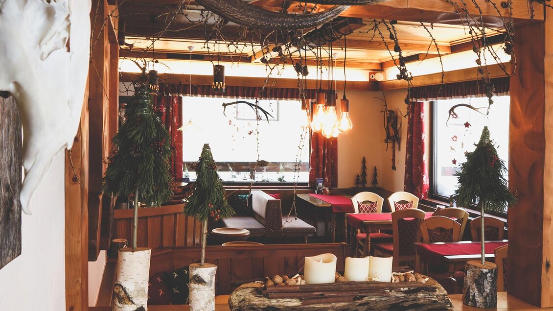 Blick in ein rustikal dekoriertes Gasthaus mit Holzdecke, Kerzen, kleinen Tannenbäumchen und Hirschgeweih an der Wand. | © Foto Tom