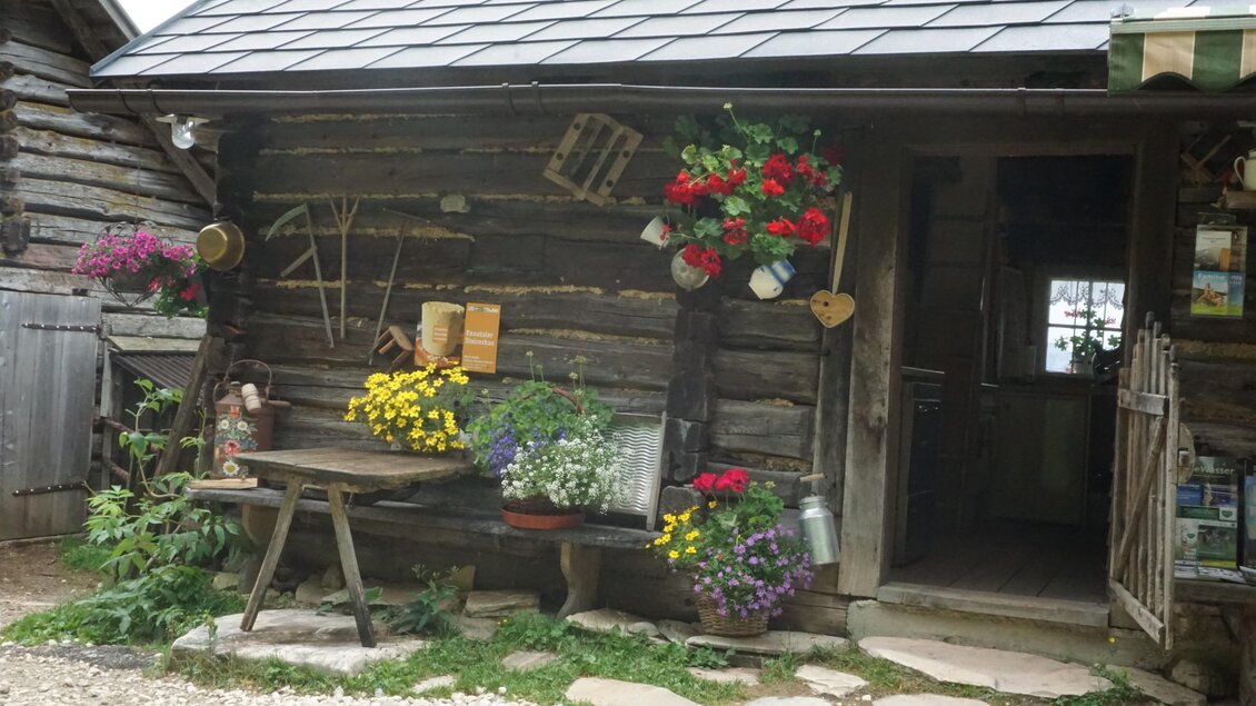 Ein rustikales Holzhaus mit bunten Blumen und Pflanzen an der Wand. Vor dem Haus steht ein Tisch und Stühle, die ein einladendes Ambiente schaffen. | © Naturpark Sölktäler