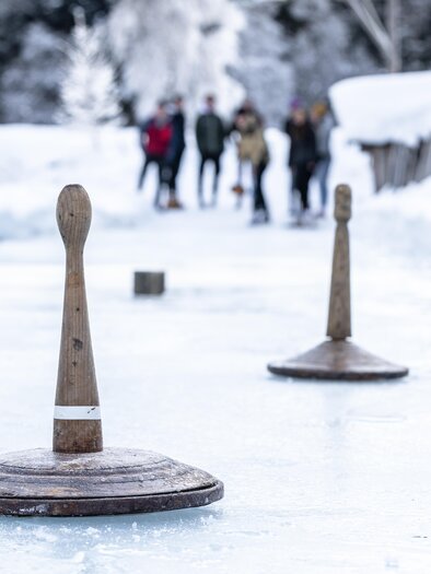 Eine winterliche Szenerie mit Eis und Holzkreisen zum Spielen. Im Hintergrund sind Menschen zu sehen, die sich amüsiert bewegen. | © Waldhäuslalm/Martin Huber