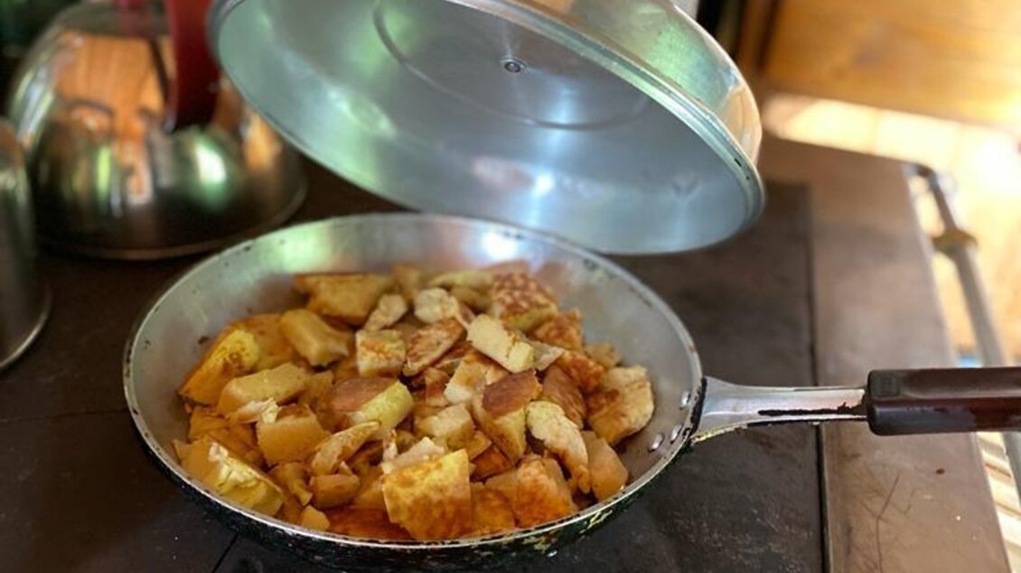 Eine Pfanne mit goldbraun gebratenen Kartoffeln wird gerade aufgedeckt. Im Hintergrund sind Küchenutensilien und eine gemütliche Küche zu sehen. | © Walhornalm