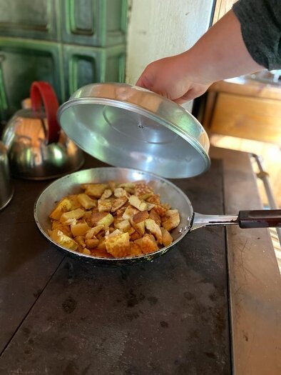 Eine Pfanne mit goldbraun gebratenen Kartoffeln wird gerade aufgedeckt. Im Hintergrund sind Küchenutensilien und eine gemütliche Küche zu sehen. | © Walhornalm