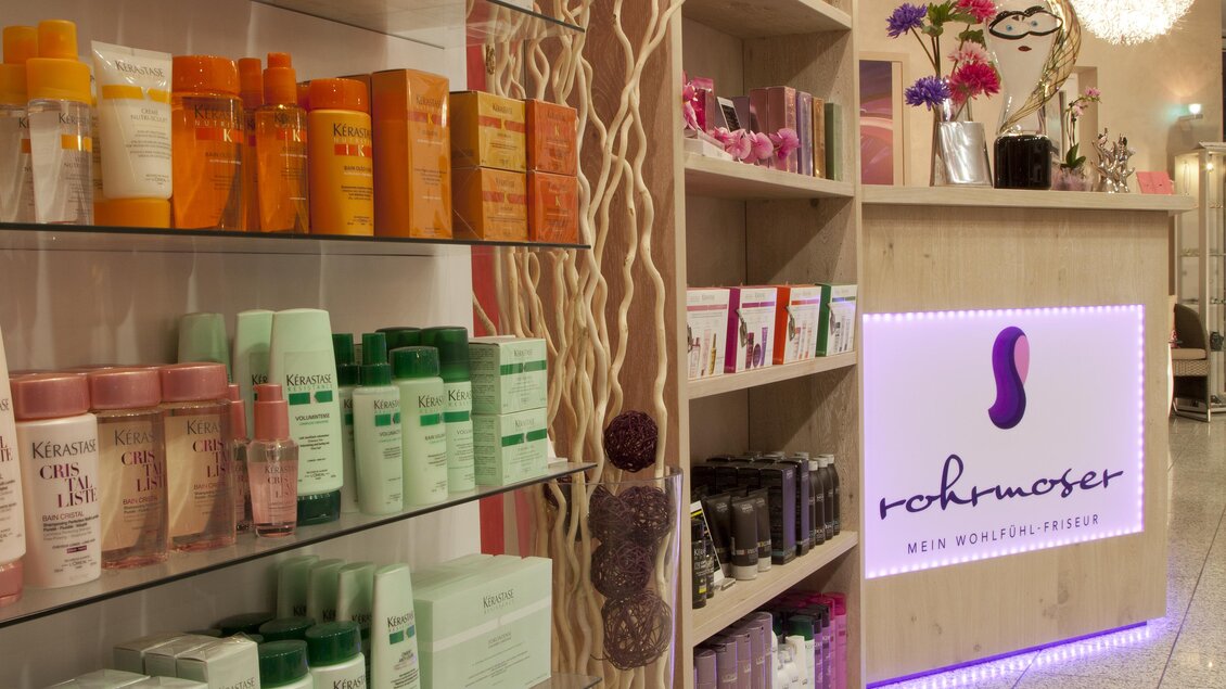 Ein modernes Geschäft mit verschiedenen Haar- und Hautpflegeprodukten auf Regalen. Der Empfangsbereich ist elegant und einladend gestaltet. | © Wohlfühlfriseur Rohrmoser