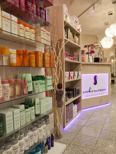 A modern store with various hair and skin care products on shelves. The reception area is elegantly and invitingly designed. | © Wohlfühlfriseur Rohrmoser