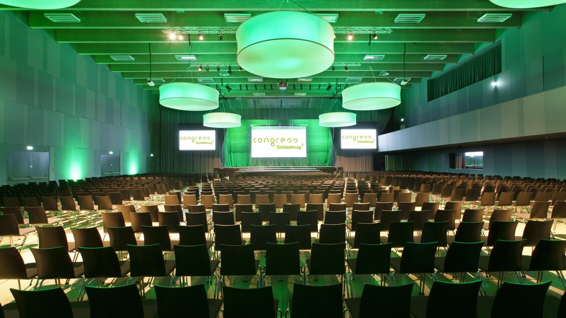 Ein großer Veranstaltungsraum mit vielen Stühlen in Reihen. Die Beleuchtung ist grün, und es gibt mehrere große Lampen an der Decke. | © Harald Steiner